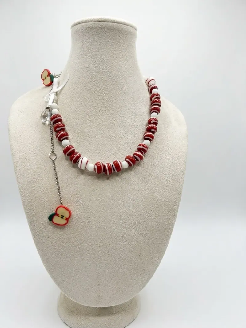 Colar de peças esmaltadas vermelhas e brancas no ródio branco, com pingente de maçã, num busto de veludo