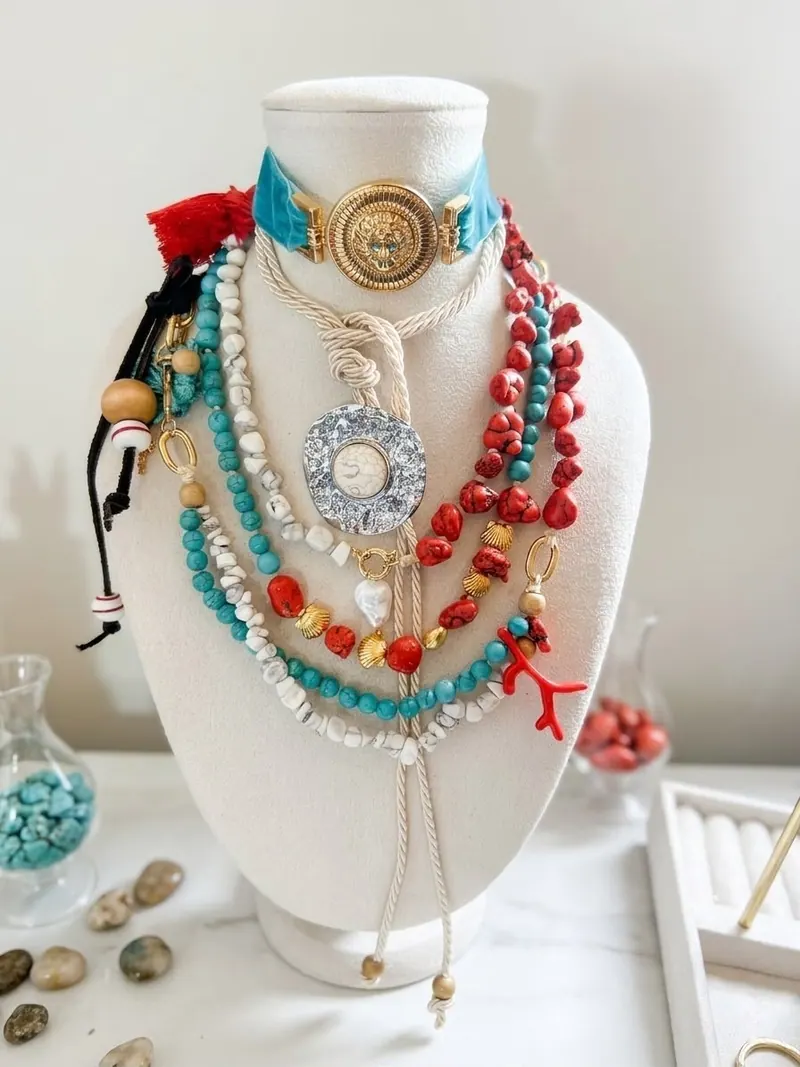 Colares de contas turquesa, vermelhas e brancas, gargantilha turquesa com medalha dourada e galho de coral, num busto