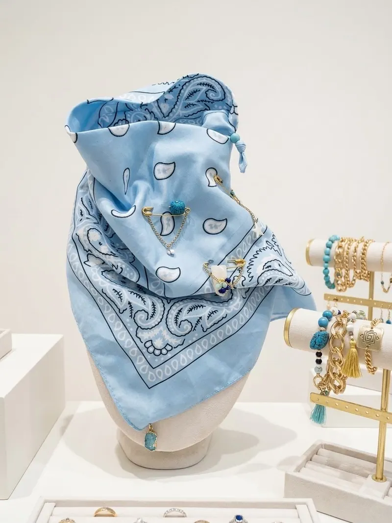Lenço azul estampado num busto, com pulseiras de contas e elos dourados ao lado