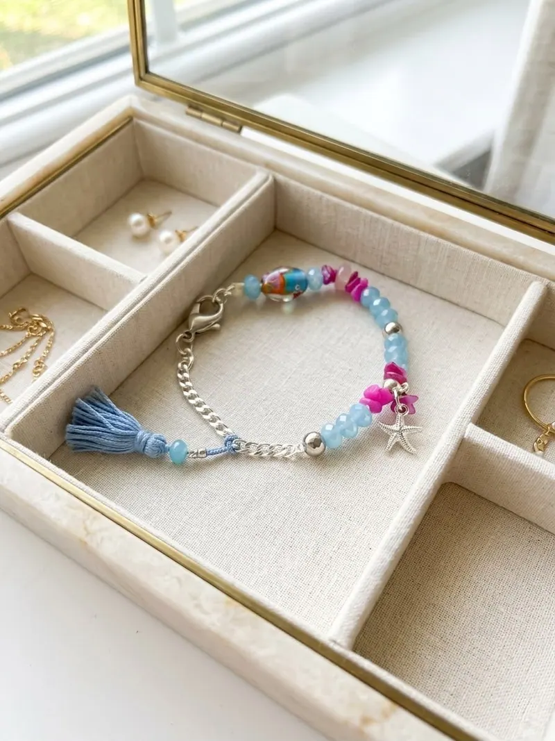 Pulseira de cristal azul claro com corrente prateada, borla azul e estrela-do-mar, numa caixa de joias