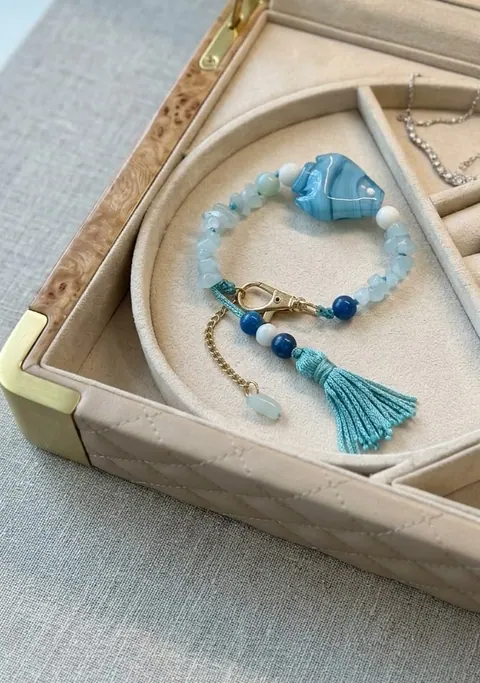 Pulseira de quartzo azul claro com peixe de vidro esmaltado e borla turquesa, numa caixa de joias